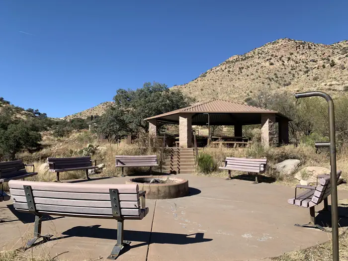 Molino — Uncovered fire pit surrounded by benches, with the covered pavilion with picnic table in the background.