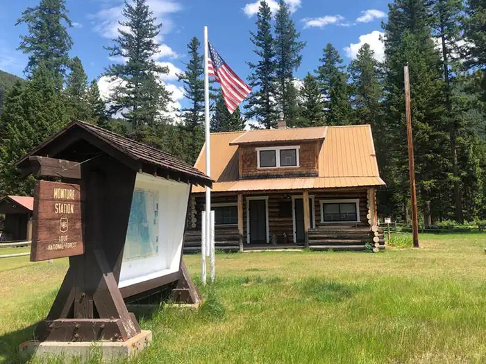 Monture Guard Station Cabin — Monture Guard Station Rental Cabin in the Summertime. An American Flag Waves in the Front Yard.