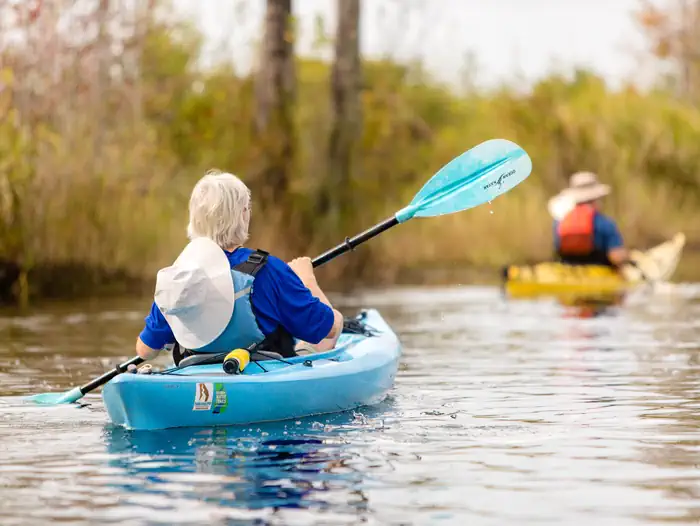 Okefenokee National Wildlife Refuge Camping — Kayaker in a blue kayak with a black and blue paddle. Second kayaker in background in a yellow kayak, wearing an orange life jacket and a brown hat.