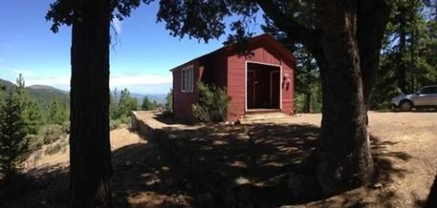 Post Creek Guard Station — Red cabin in between trees with blue sky in background.