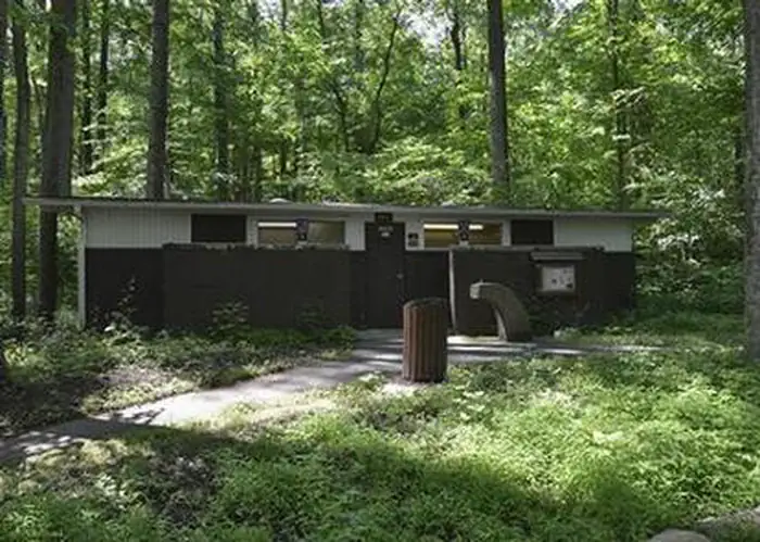 Owens Creek Campground — Front view of upper comfort station building showing 2 windows, door and paved path. Dense deciduous forest visible behind building