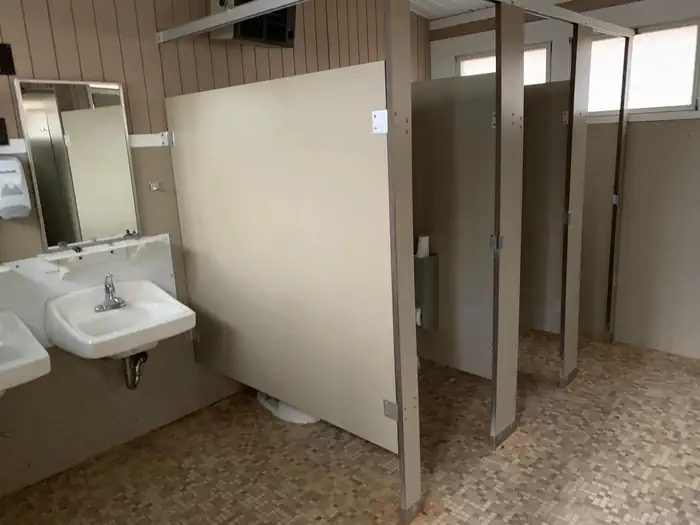 Owens Creek Campground — Partial interior view of comfort station. 2 small bathroom stalls, 2 windows, 2 porcelain sinks with mirrors. Flooring is tile,