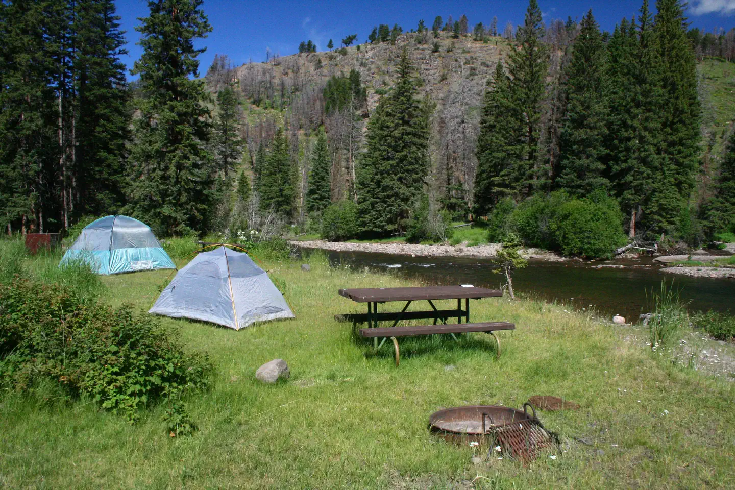 Slough Creek Campground — Two tents pitched at a campsite with a firepit and picnic table along Slough creek