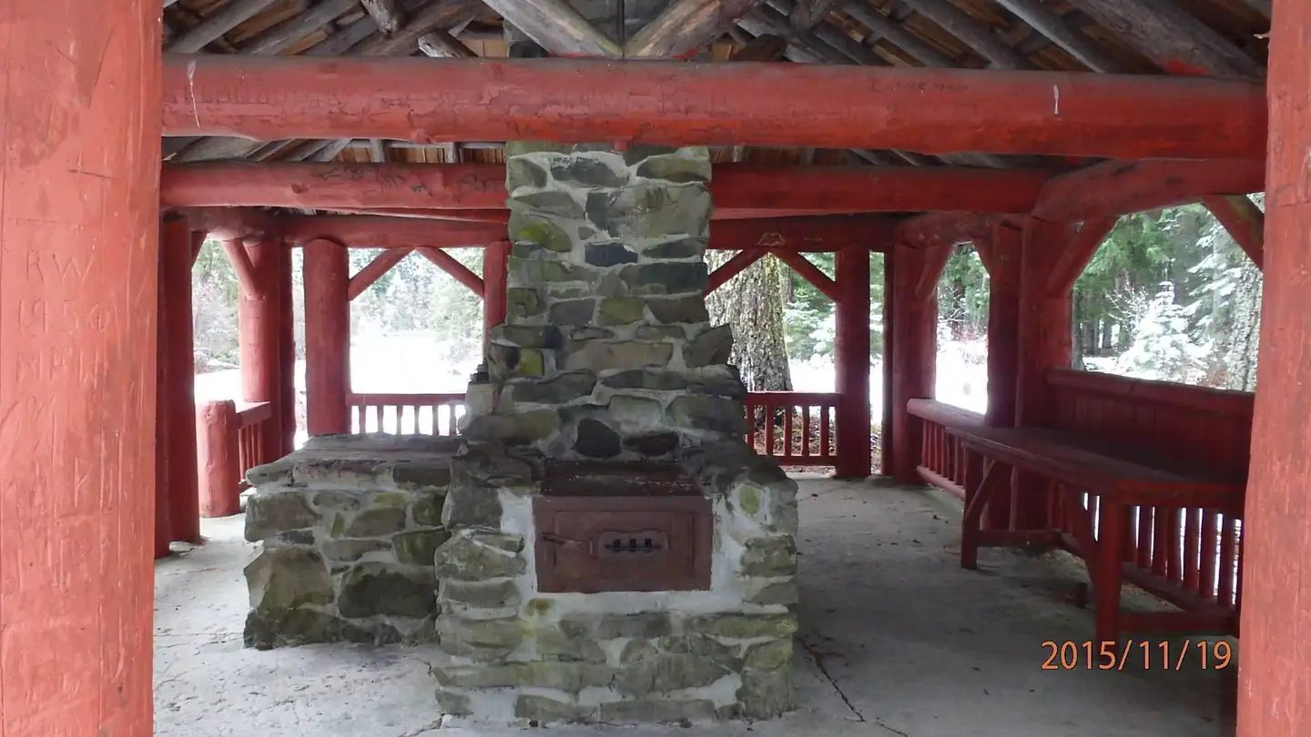 American Forks Campground — Stone fireplace and chimney next to counter under red-painted log shelter.