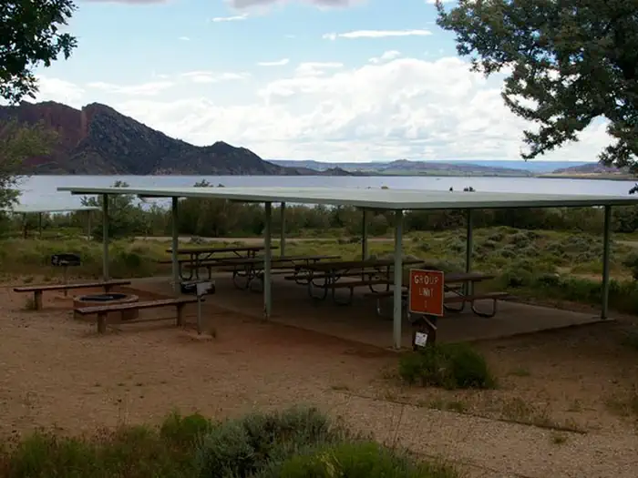 Lucerne Campground - Ashley National Forest — Pavillion over picnic tables in a group area. There is a firepit with benches and two grills off to the side.