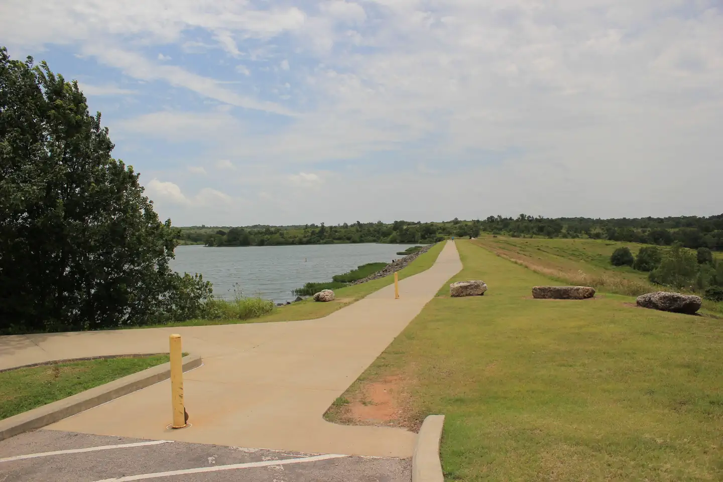 Rock Creek Campground - Chickasaw National Rec Area — A view of the dam area and trail on Veteran's Lake under a blue sky with cirrus clouds