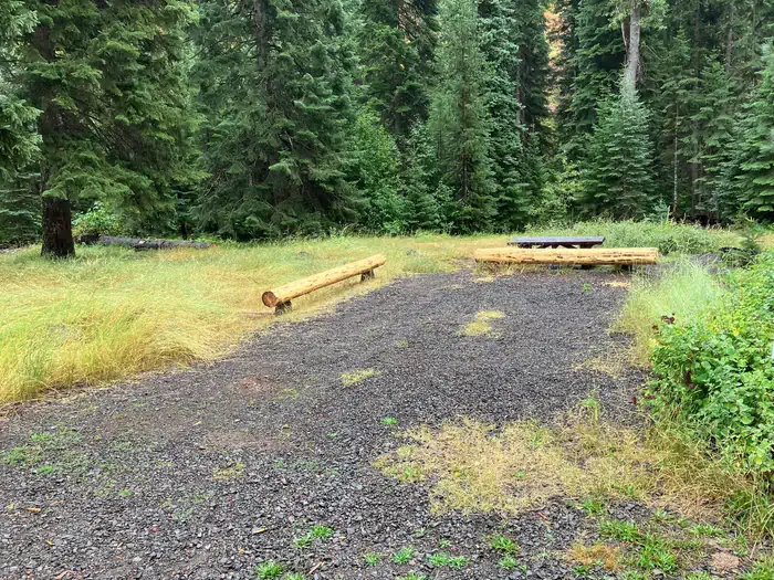 North Fork Catherine Creek Campground — Gravel parking pad with new log barriers and picnic table. Stream in the background.