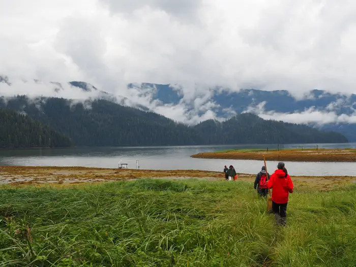 Harding River Cabin β Harding River Cabin scenery, four people walking along grassflats to a boat with a river and clod covered mountains in background