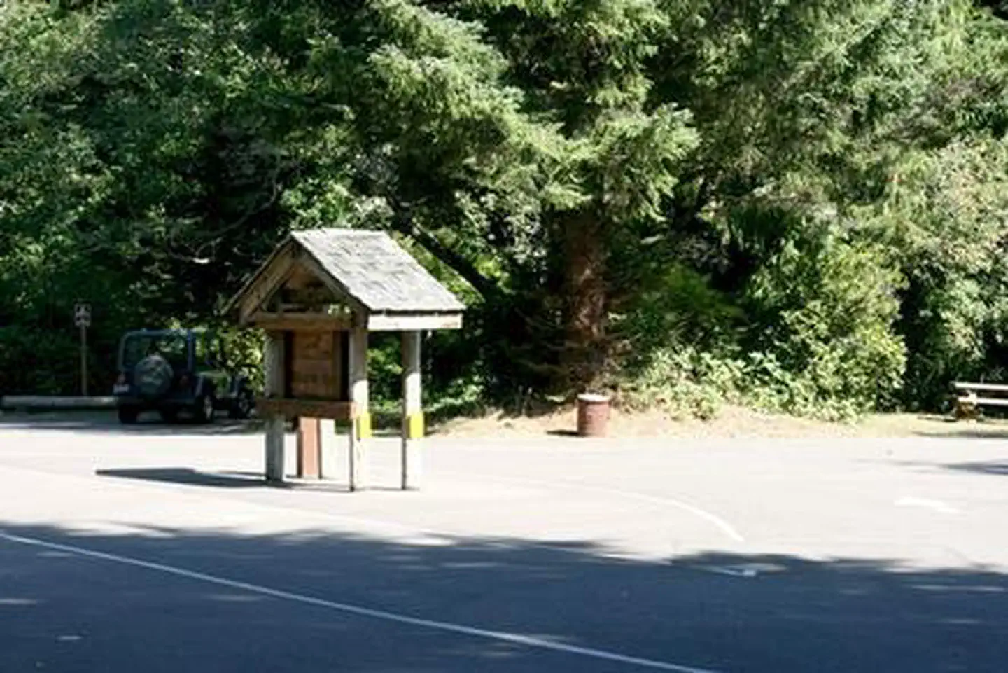 Tahkenitch Campground — Paved entry with kiosk and fee tube in front of parking area and large evergreen shrub tree.