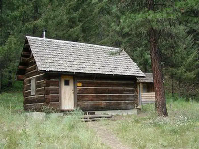 Teanaway Guard Station — Small log cabin next to pine tree in open glade in front of conifer forest.