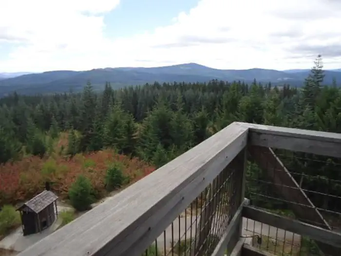 Clear Lake Cabin Lookout — View from lookout deck over outhouse with mountains and forest in the background.