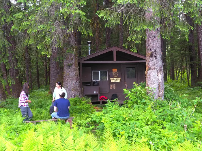 Eagle Lake Cabin — Three people outside brown cabin with trees and ferns