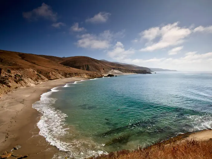 Santa Rosa Island Backcountry Beach Camping — Sandy beach with ocean and small waves and steep coastal bluffs covered in dry grass. 