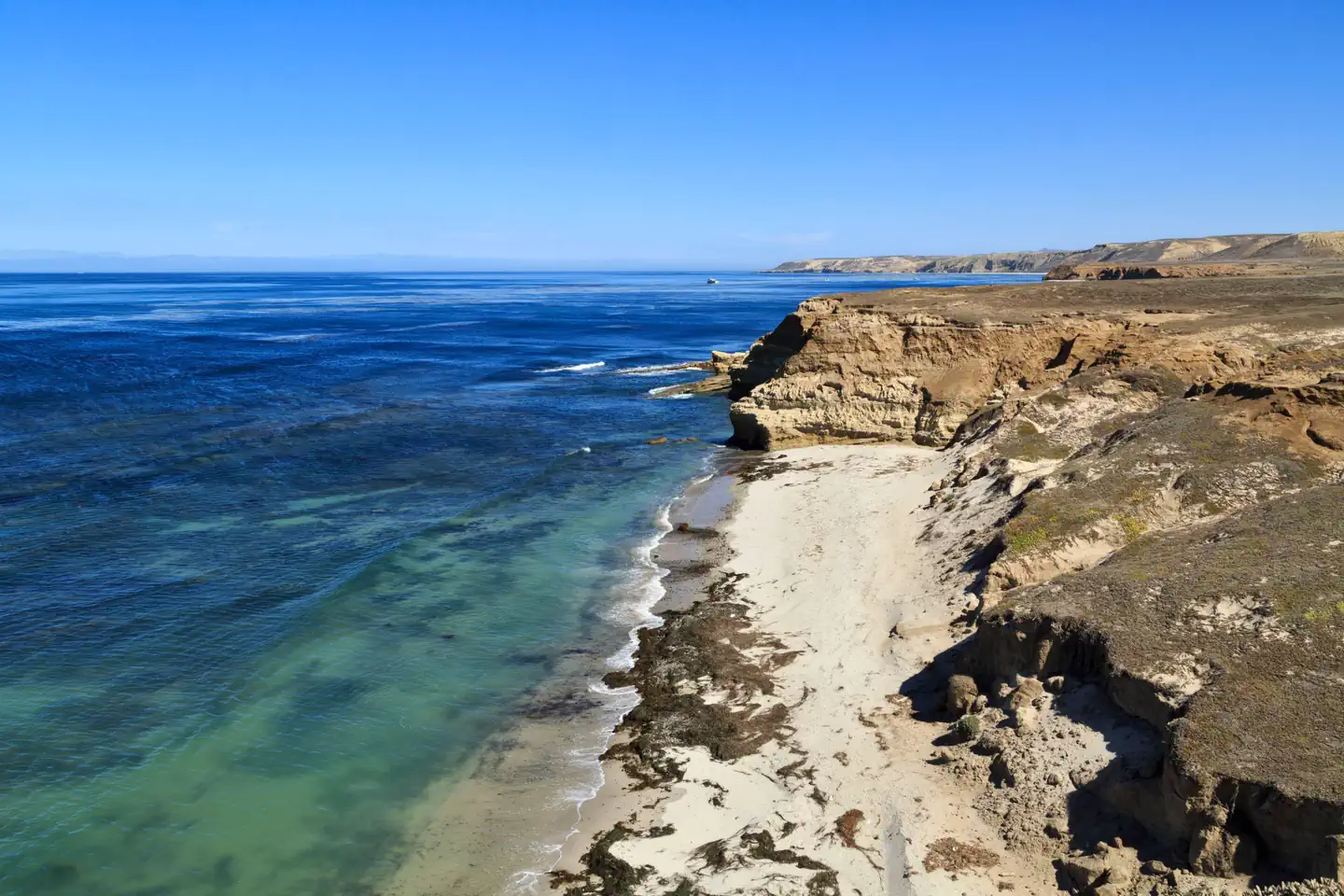 Santa Rosa Island Backcountry Beach Camping — Sandy beach with ocean, small waves and steep coastal bluffs covered in dry grass.