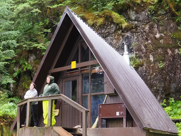 Mount Flemer Cabin — Two people by railing of entrance to Mount Flemer Cabin with trees in background