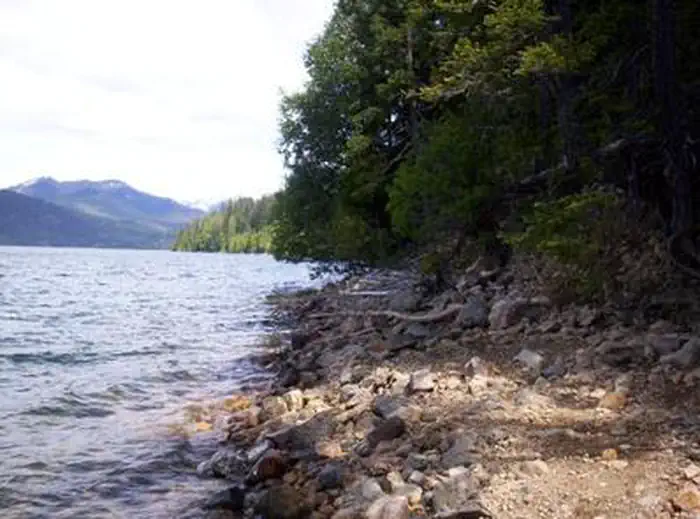 East Kachess Group Site — Looking from narrow, rocky lake shore lined with trees over choppy water to a far off mountain under bright, cloudy sky.