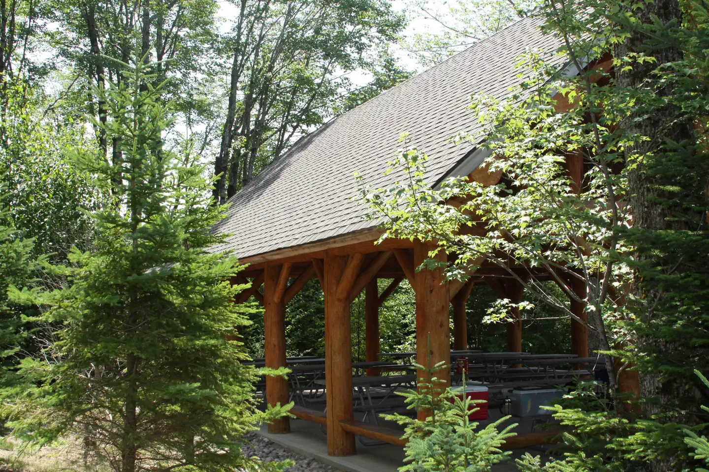 Schoodic Woods Campground — Exterior view of log cabin style picnic pavilion surrounded by spruce and pine trees.
