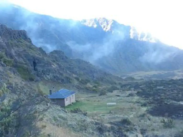 Haleakala National Park (cabin Permits) — view from above of cabin against a sloping cliff, fog drifting in the background