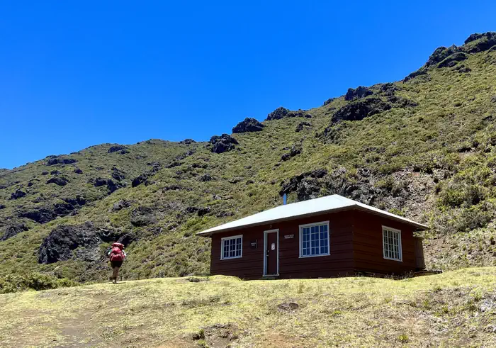 Haleakala National Park (cabin Permits) — backpacker walks up to cabin at the base of a hill