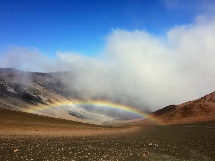 Haleakala National Park (cabin Permits) — view of crater, orange and black cinder hills with clouds and a low rainbow 
