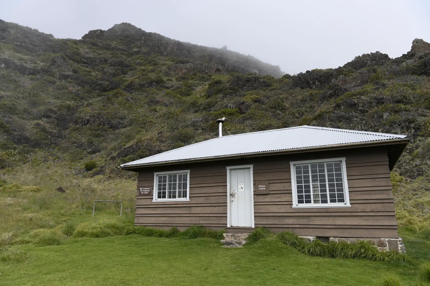Haleakala National Park (cabin Permits) — view of cabin surrounded by grass and tall cliff behind