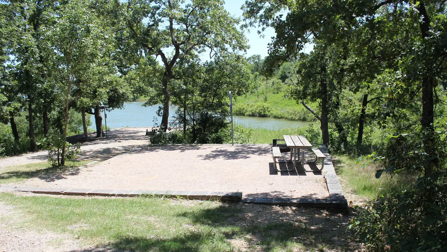 The Point Campground (ok) Chickasaw Nra — a square campground mostly in sunlight, with a wooden picnic table at the far right.