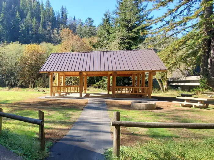Castle Rock Group Campground β Large flat field. Tents and picnic tables in front of a road and large conifer treein the back, fire ring and picnic table behind single pole fence in foreground.
