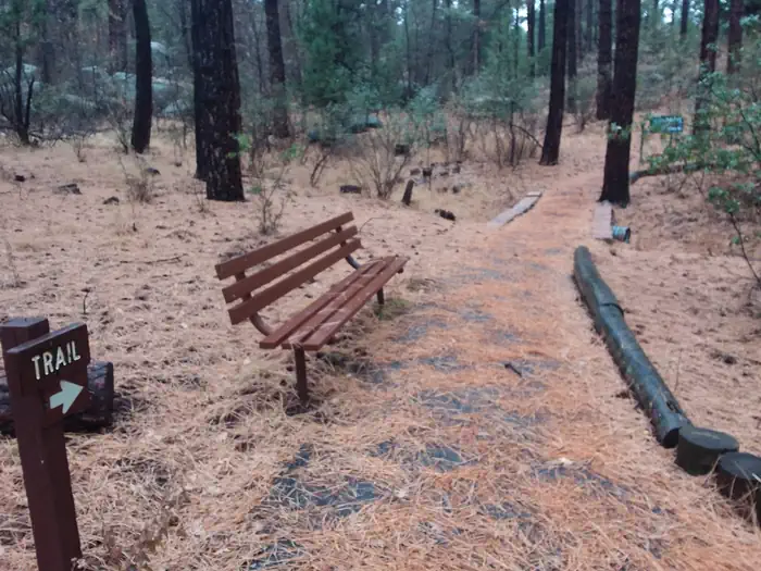 Groom Creek Schoolhouse β Lion's accessible paved interpretive trail bench and directional sign post leading to wooden bridge with rustic railing.