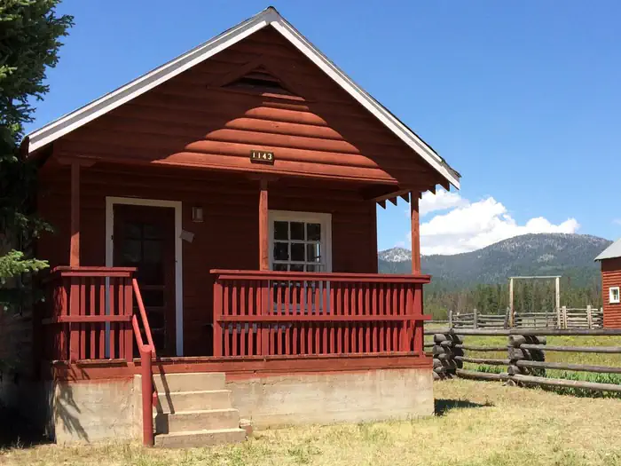 Paddy Flat Guard Station — Paddy Flat Guard Station East - front of rustic cabin showing porch and stairs with blue skies and mountains beyond
