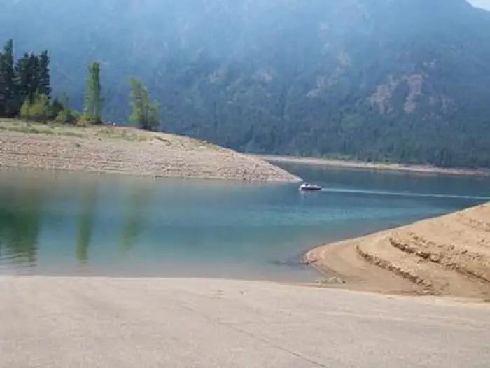 Wish Poosh Campground — View of boat ramp leading into lake with sloped earthen banks, looking beyond to a small boat and tree covered slopes above high water line.