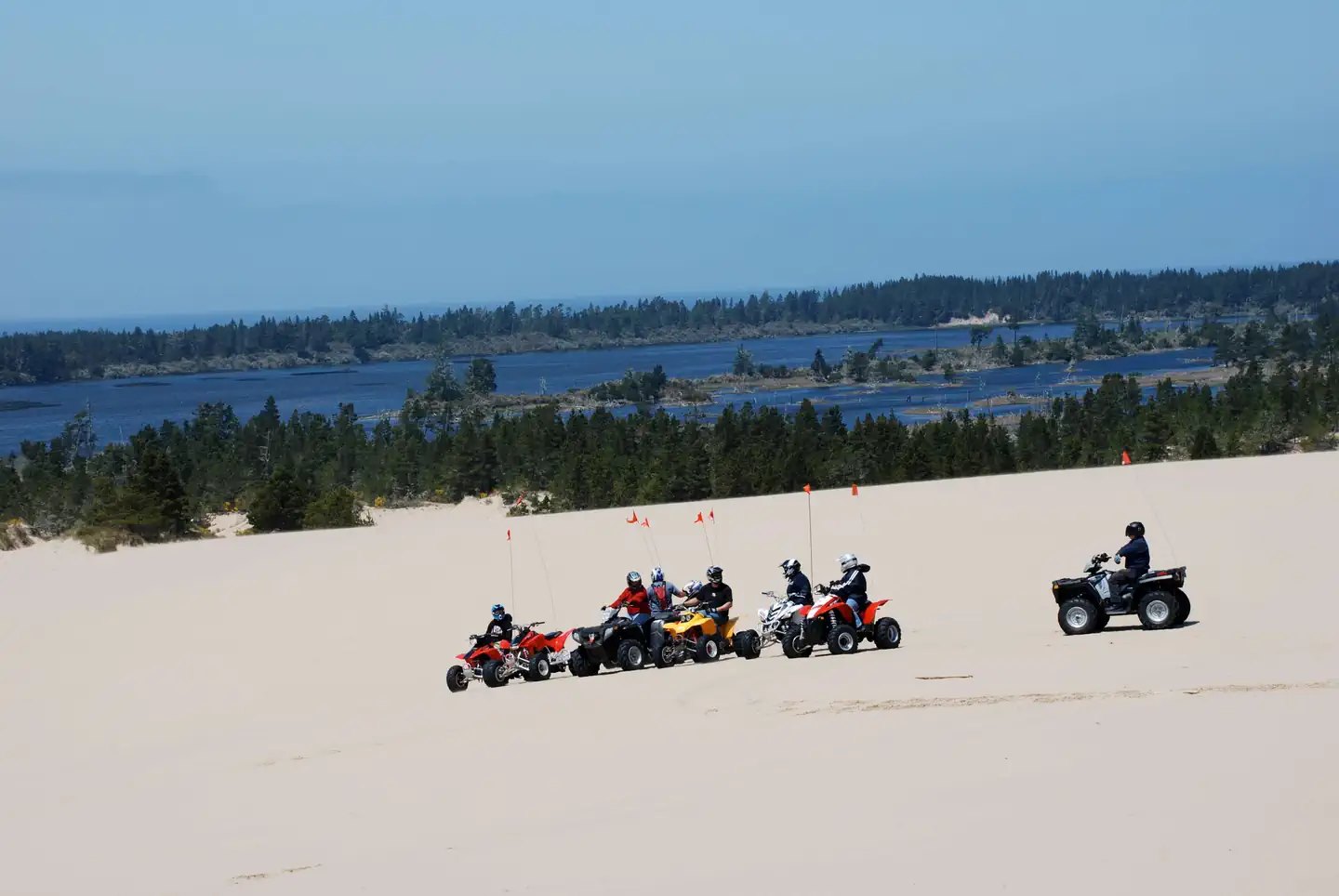Horsfall Campground — Off road vehicles on flat expanse of sand in front of blue lake ringed by conifer trees.