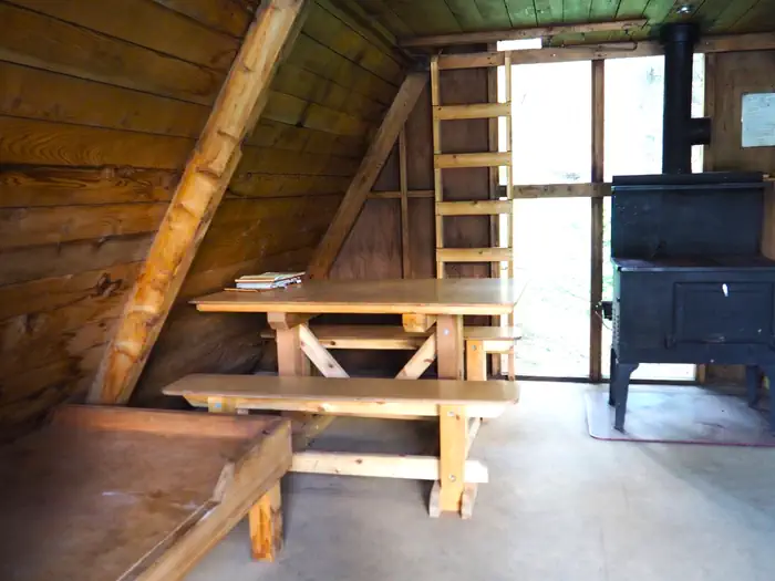 Mount Rynda Cabin — Mount Rynda Cabin interior showing wood table and bed with stove and ladder to loft