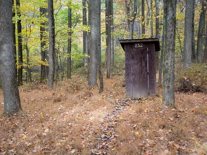 Adirondack Shelters — Small enclosed wooden pit toilet building. Surrounded by trees in late fall.