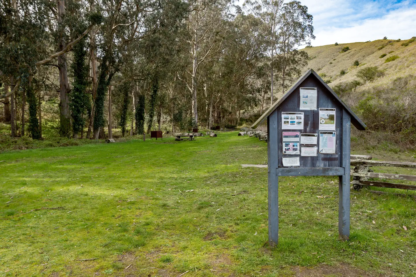 Haypress Campground — A bulletin board with signs in a meadow. Picnice tables and food lockers are in the background. The campground is lined with trees.