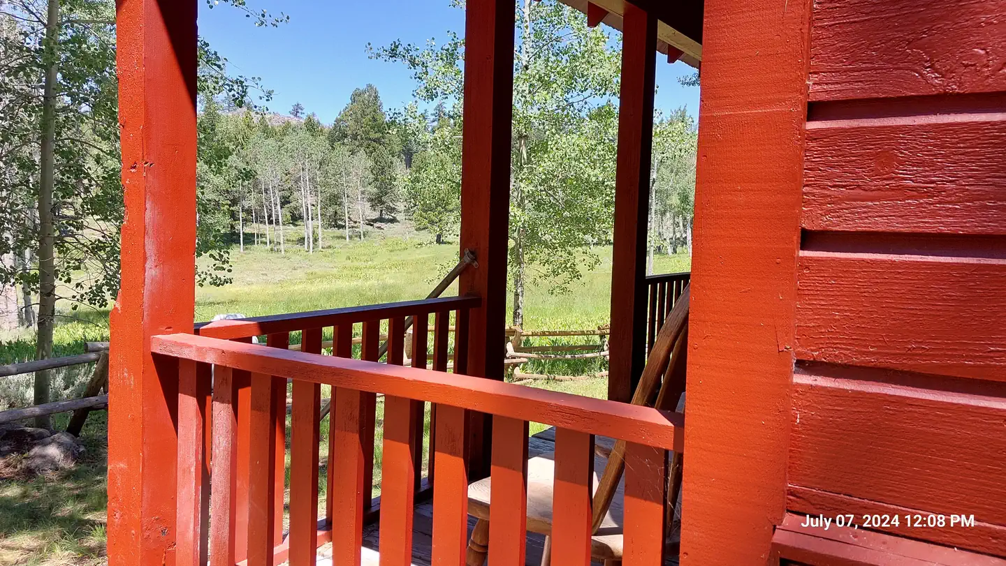 Patterson Guard Station — bright red wooden rails frame the front porch of the guard station where a wooden chair offers a view of the adjacent meadow on a sunny day.