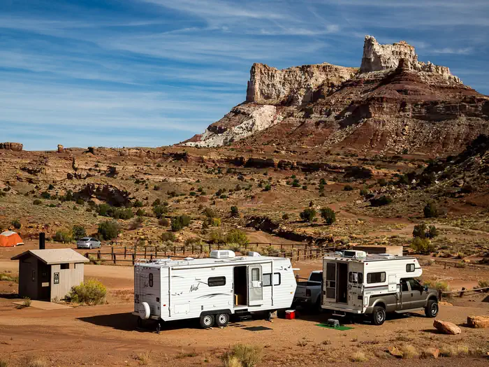 Temple Mountain Townsite Campground — An RV and truck camper are parked in a campground below a large sandstone butte.