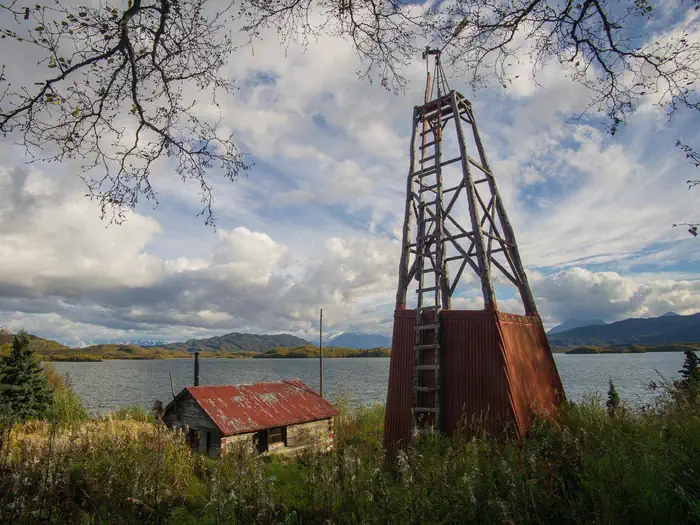 Fure's Cabin — View of a wood cabin and windmill in a grassy field with a lake and mountains in the background.