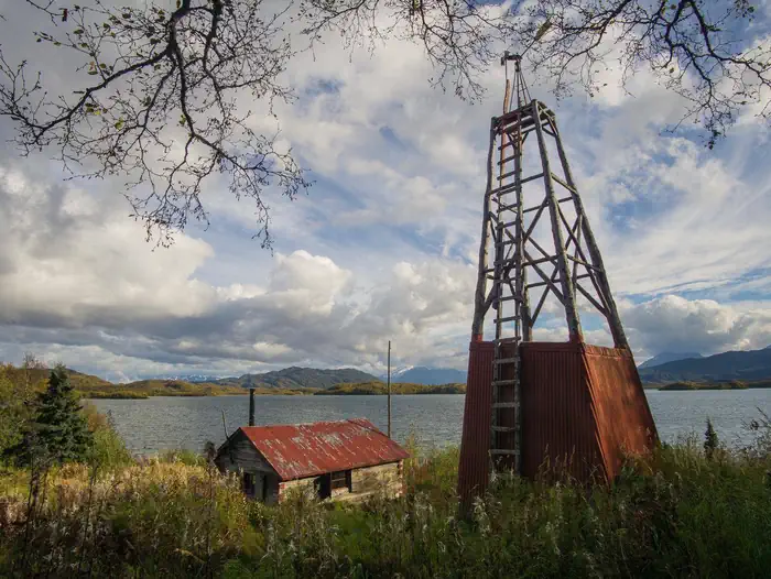 Fure's Cabin — View of a wood cabin and windmill in a grassy field with a lake and mountains in the background.