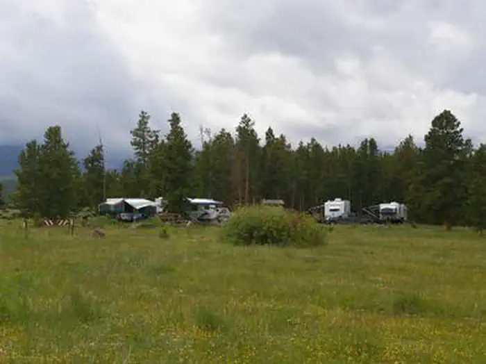 BROWNE LAKE GROUP SITES — Trucks and trailers in a group campground with a grassy meadow and pines in the background.
