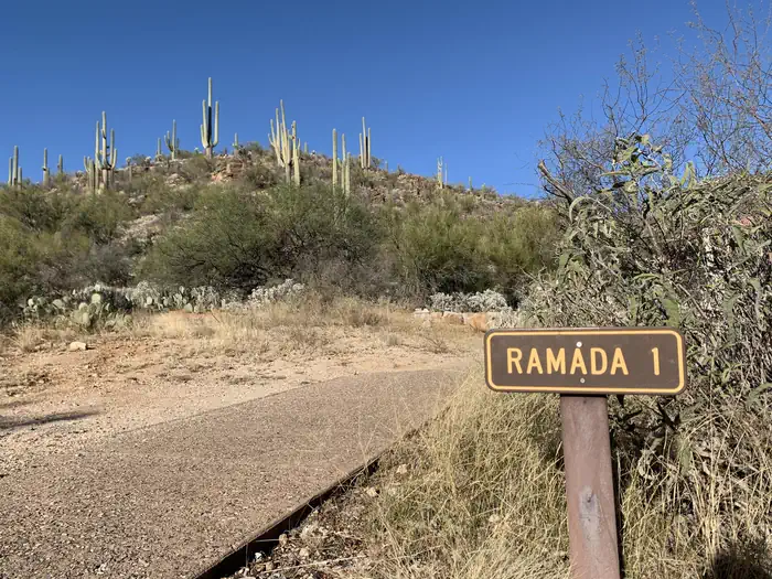 SABINO CANYON RECREATION AREA CACTUS RAMADA 1 — Paved path to the left of a sign saying "Ramada 1"