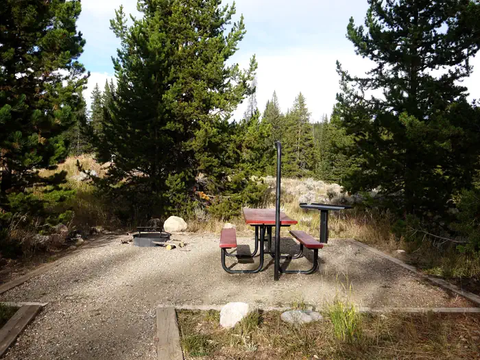 BOULDER PARK CAMPGROUND — Picnic table, fire ring and grill set in the middle of a pine forest.