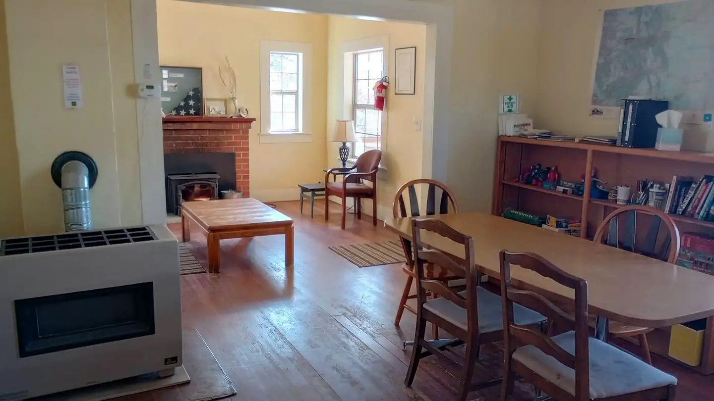 Upper Crossing Guard Station — View of living room and dining room. Table has 4 chairs (more in storage), shelf equipped with First Aid kit, history/diary booklets, toys/games, and miscellaneous books.