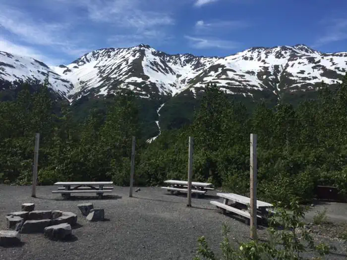 Spencer Glacier Whistle Stop Group Campground — Centralized area with picnic tables, campfire ring, and poles for hanging tarps.