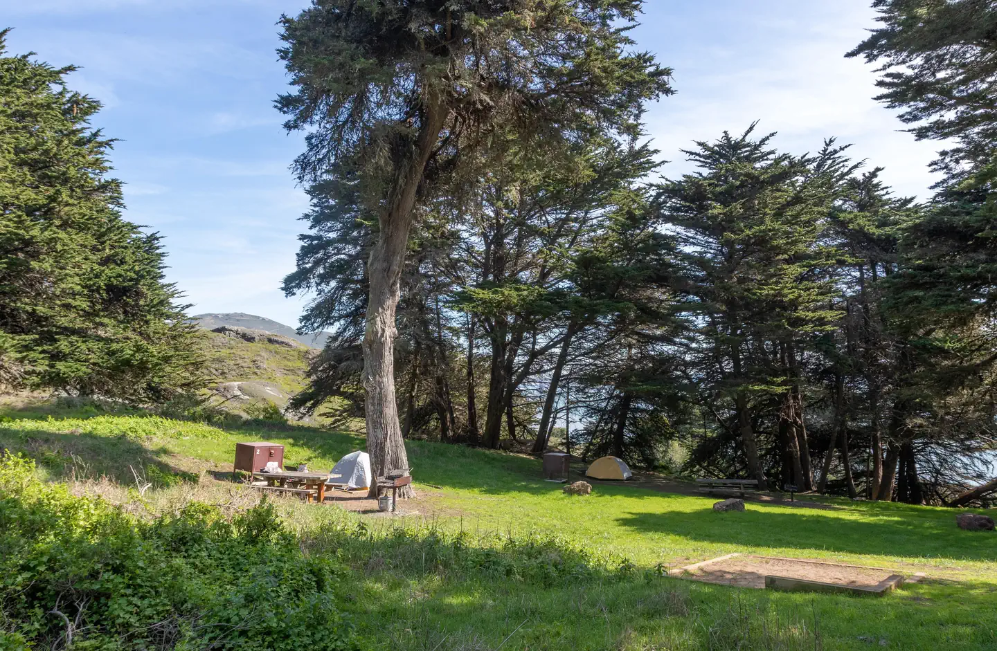 BICENTENNIAL CAMPGROUND — Side view of Bicentennial Campground. In the foreground is Site 1, to the left is Site 2, and in the background is Site 3. Through the cypress trees you can see the hills of the headlands.