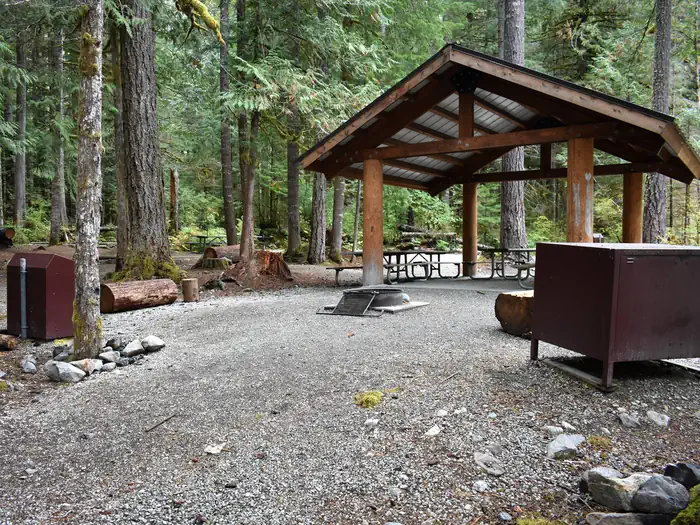 UPPER GOODELL GROUP CAMPGROUND β Shelter provided rain and sun protection to several picnic tables located underneath. Campfire ring and food storage lockers in foreground.