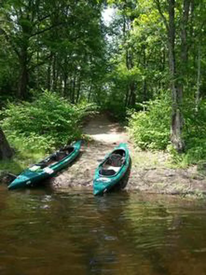 Alosa Campsites — Two green kayaks on shore of river with trees in the background