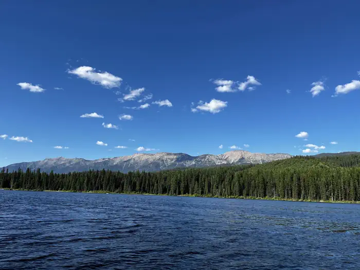 Lake Alva Campground — A photo of Lake Alva on a sunny day. The water and skies are bright blue, and trees and the swan range can be seen in the background.
