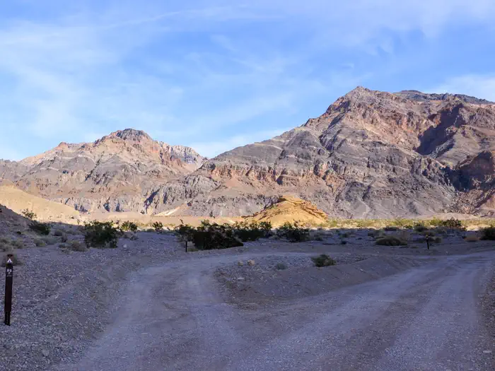 Death Valley Backcountry Roadside Camping — Gravel dirt road with parallel roadside campsite shaded in the foreground, sunny mountains in the background.