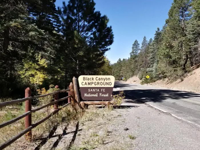 Black Canyon Campground (santa Fe National Forest, Nm) — A campground sign with the words Black Canyon with a road and trees in the background.
