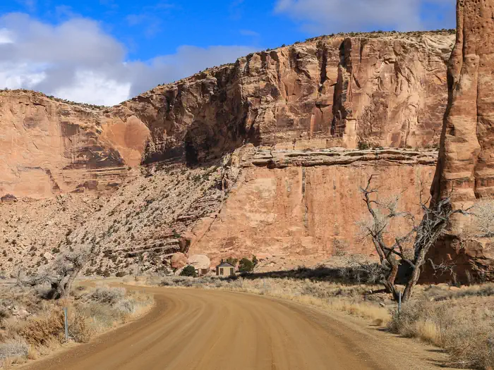 Buckhorn Draw — A dirt road cuts through a wide canyon of orange cliffs with a bathroom in the distance.